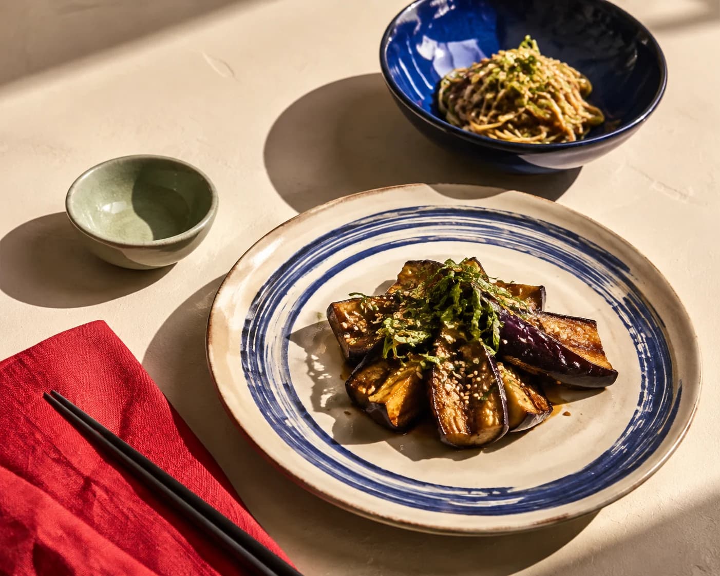 Illustrative Japanese-style table with a cobalt-ringed plate, blue noodle bowl, and vermilion linen